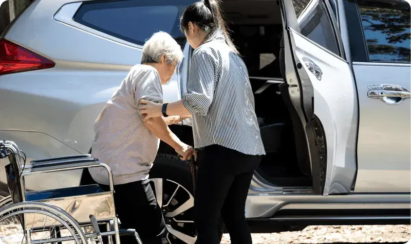 Caregiver helping an older woman step into a car for an ambulatory medical ride